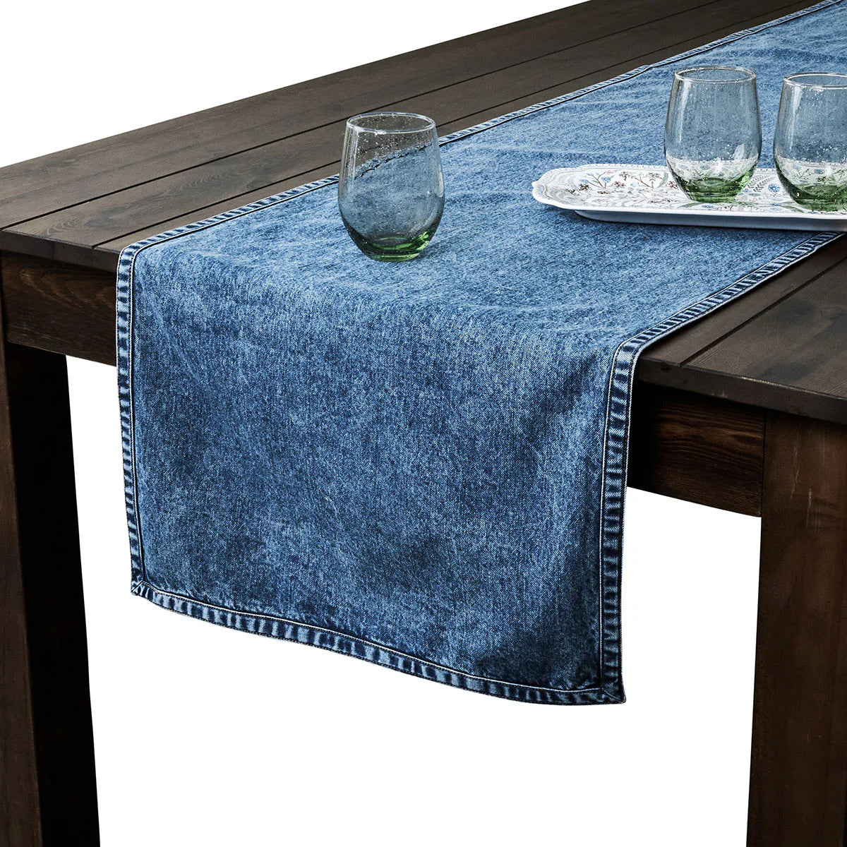 Blue denim table runner on a wooden table with glasses and a plate.