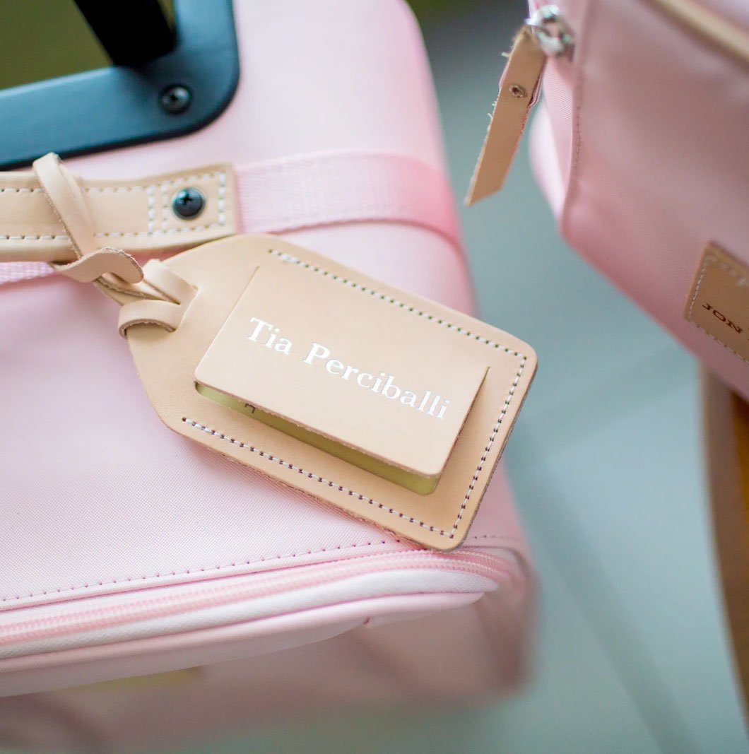 A pink leather luggage tag with a clear plastic slot containing an address card, attached to a suitcase.