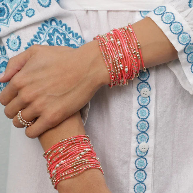 Close-up of hands wearing multiple coral beaded bracelets on a light fabric background.