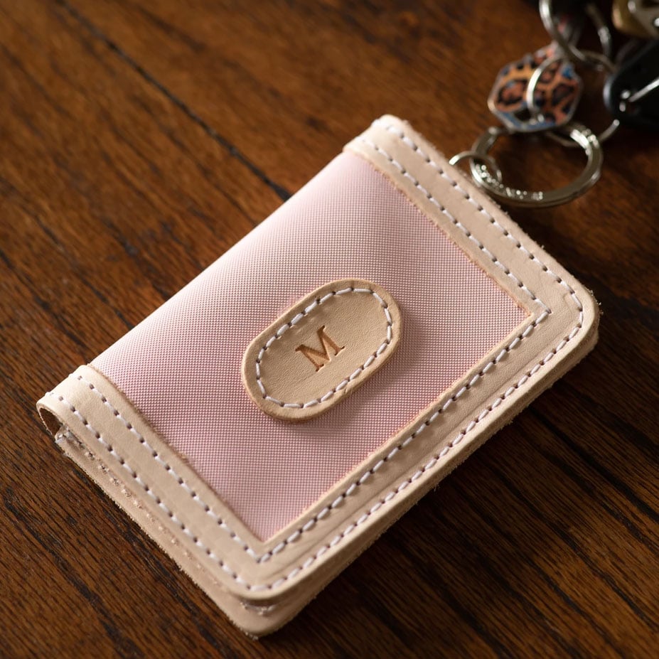 A pink and beige ID wallet with leather trim, a key ring attached, and a snapped closure.