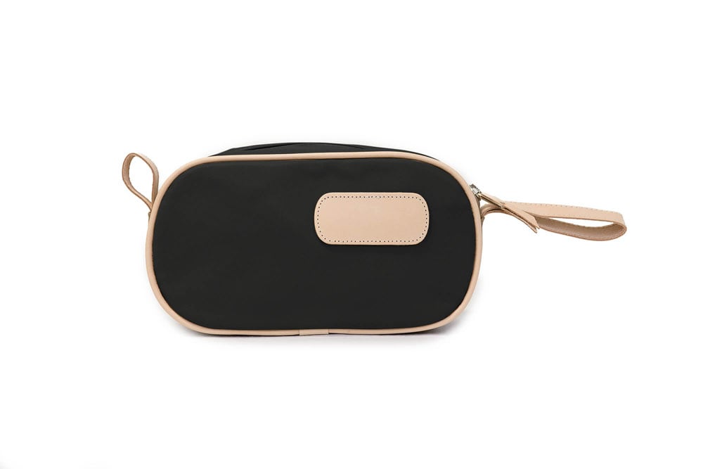 A person holding a black and brown vinyl coated canvas shaving kit with natural leather trim and straps, featuring a zippered closure and the brand name 'Lewis' on the front.