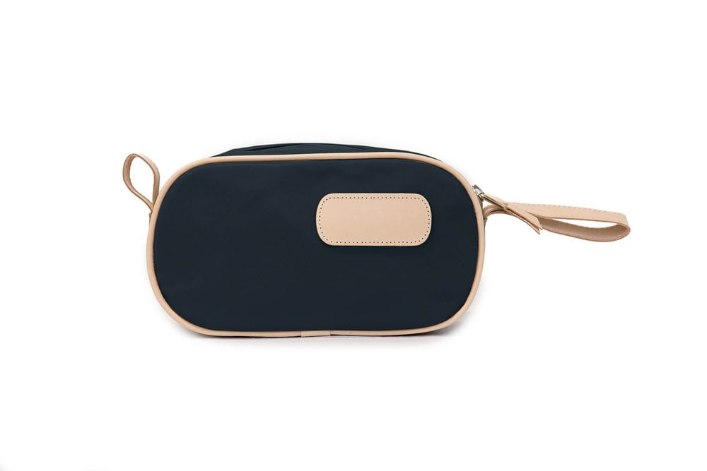 A person holding a black and brown vinyl coated canvas shaving kit with natural leather trim and straps, featuring a zippered closure and the brand name 'Lewis' on the front.