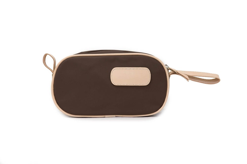 A person holding a black and brown vinyl coated canvas shaving kit with natural leather trim and straps, featuring a zippered closure and the brand name 'Lewis' on the front.