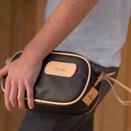 A person holding a black and brown vinyl coated canvas shaving kit with natural leather trim and straps, featuring a zippered closure and the brand name 'Lewis' on the front.